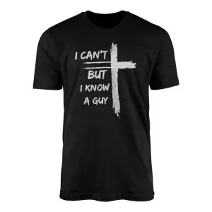 Distressed white brushstroke Christian cross beside I Can't But I Know A Guy lettering on a black flat lay t-shirt