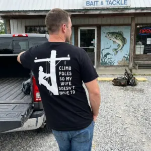Funny Lineman Husband Climb Poles T-Shirt 11 Outdoor lifestyle view showing the back print with utility pole climber graphic and text.