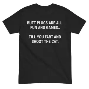 The back of a black t-shirt laid flat, featuring the white text "BUTT PLUGS ARE ALL FUN AND GAMES.. TILL YOU FART AND SHOOT THE CAT.