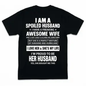 Back of a black t-shirt laid flat with white text stating I am a spoiled husband with a freaking awesome wife.