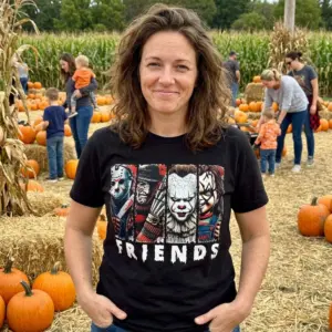 Horror Movie Characters Friends T-Shirt 11 Individual in a black Horror Friends T-Shirt enjoying a Halloween gathering, surrounded by seasonal decorations.
