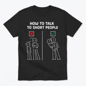 Flat lay of a black t-shirt printed with a funny short people meme showing the right and wrong way to talk to short people.