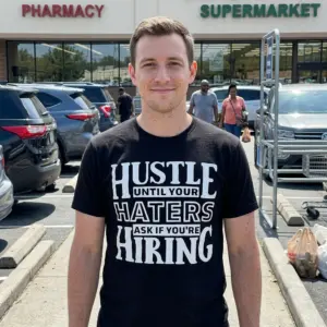 Hustle Until Your Haters Ask If You're Hiring T-Shirt 11 Person wearing a black shirt with white lettering: 'Hustle Until Your Haters Ask If You're Hiring'.