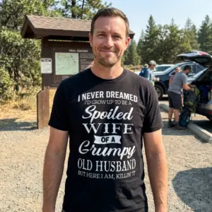 Spoiled Wife of a Grumpy Husband T-Shirt 10 Lifestyle image of T-shirt with a humorous quote, outdoor context.
