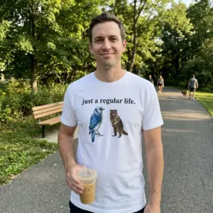Just A Regular Life Blue Jay And Raccoon Funny White T-Shirt 11 Close-up casual look showcasing white tee and white tee front print reading JUST A REGULAR LIFE above a realistic watercolor blue jay and standing brown