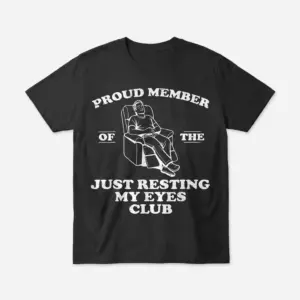 Flat lay front view of a Just Resting My Eyes Shirt featuring a graphic of a man napping in a recliner.