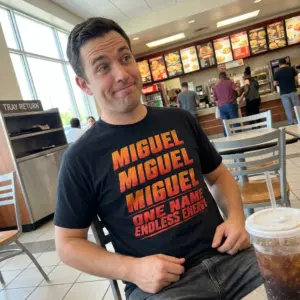 Miguel One Name Endless Energy Distressed Graphic Black T-Shirt 10 Everyday streetwear outfit styling black shirt with black tee front print reading MIGUEL three times in distressed orange red gradient above ONE NAME