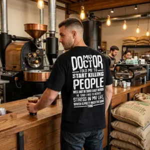 My Doctor Told Me To Reduce Stress Sarcastic Back Print Tee 10 Man wearing a black T-shirt with a large white sarcastic doctor and stress message across the back in a coffee shop.