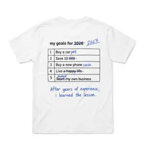 Flatlay white t-shirt featuring back print of a 5-row table reading my goals for 2026 edited to 2027 in blue pen with funny realistic edits