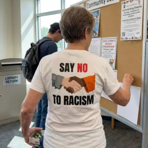 Say No to Racism Handshake Parody Graphic T-Shirt 11 Close-up casual look showcasing white tee and back print reading SAY NO TO RACISM with two hands shaking in grey and orange sleeves
