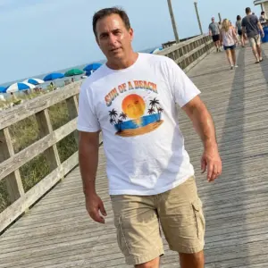 Sun Of A Beach Retro Sunset Island Palm Trees Pun T-Shirt 11 Close-up casual look showcasing white tee and white tee front print reading SUN OF A BEACH in retro arch text over a tropical sunset island
