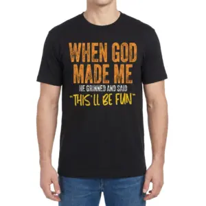 When God Made Me Funny Christian T-Shirt 9 Man wearing a black t-shirt printed with "When God Made Me He Grinned And Said 'This'll Be Fun'" across the chest.